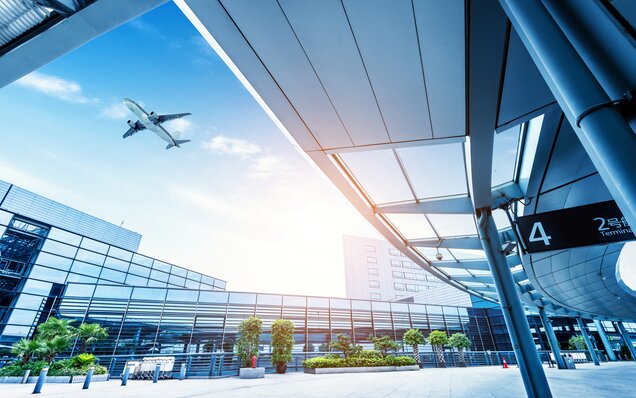 Flugzeug im Anflug über modernen Flughafen-Terminal mit großflächigen Glasfassaden